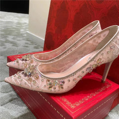 Pink high-heeled shoes with crystal embellishments on a red box.