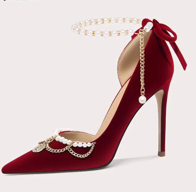 Red high-heeled shoe with gold chain and pearl decorations on a light gray background