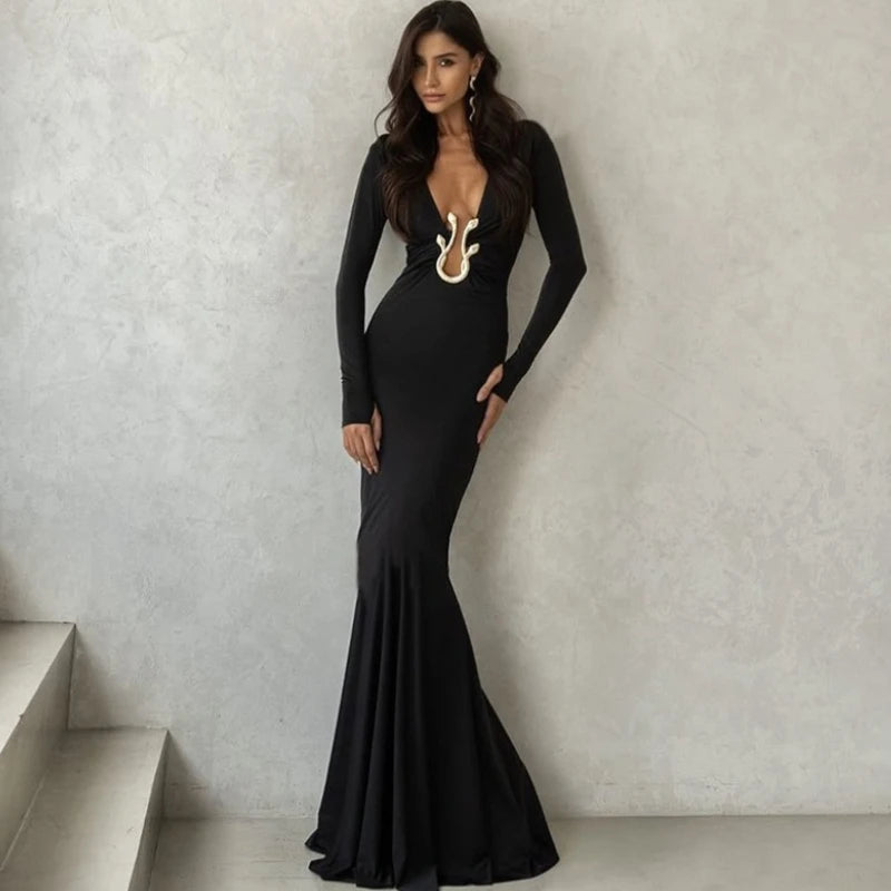 Woman in a black evening gown with gold accents standing against a light gray wall.
