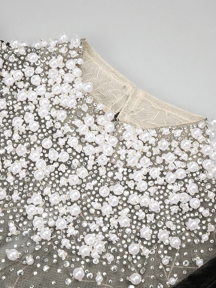 Close-up of a fabric with white pearls and gold embroidery on a gray background