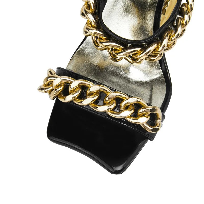 Black high-heeled shoe with gold chain detail on a white background