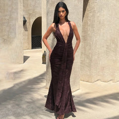 Woman in a deep-neck, dark brown dress standing in front of a stone building.