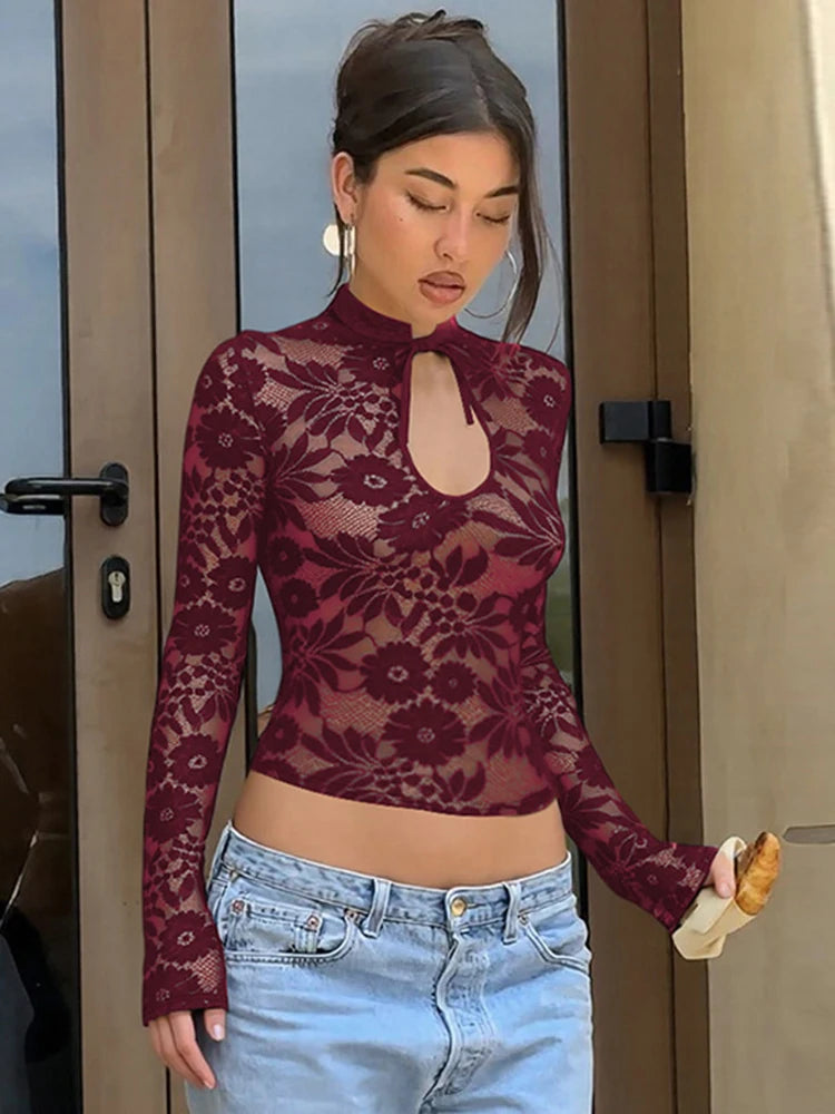Woman wearing a sheer maroon lace top and light blue jeans standing in front of a door.