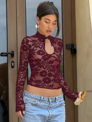 Woman wearing a sheer maroon lace top and light blue jeans standing in front of a door.