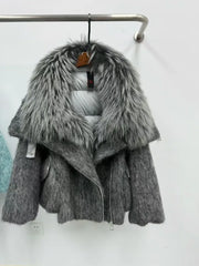 Gray knitted jacket with fur collar on a hanger against a white wall.