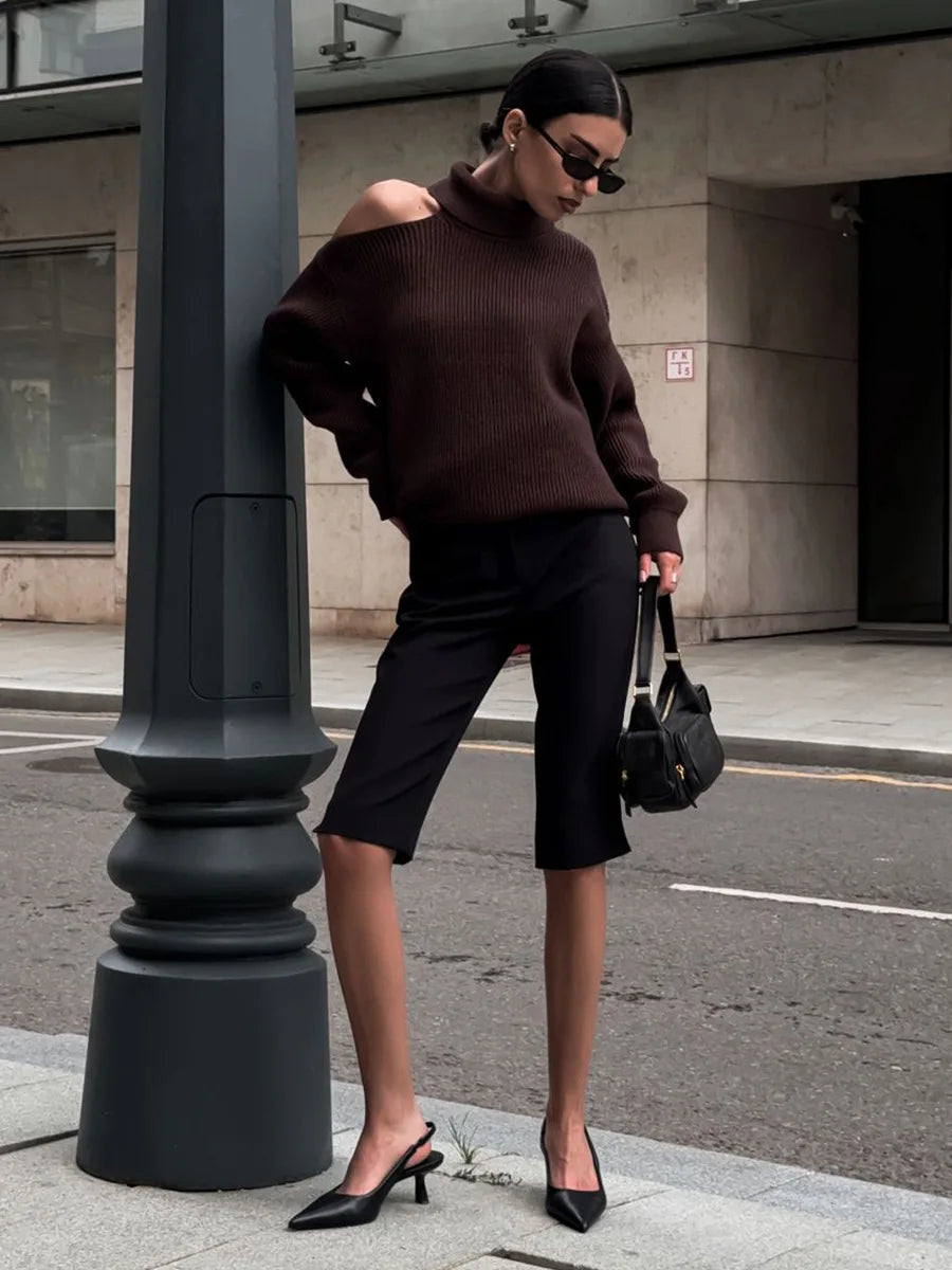 Woman in a brown sweater and black pants standing on a city street.