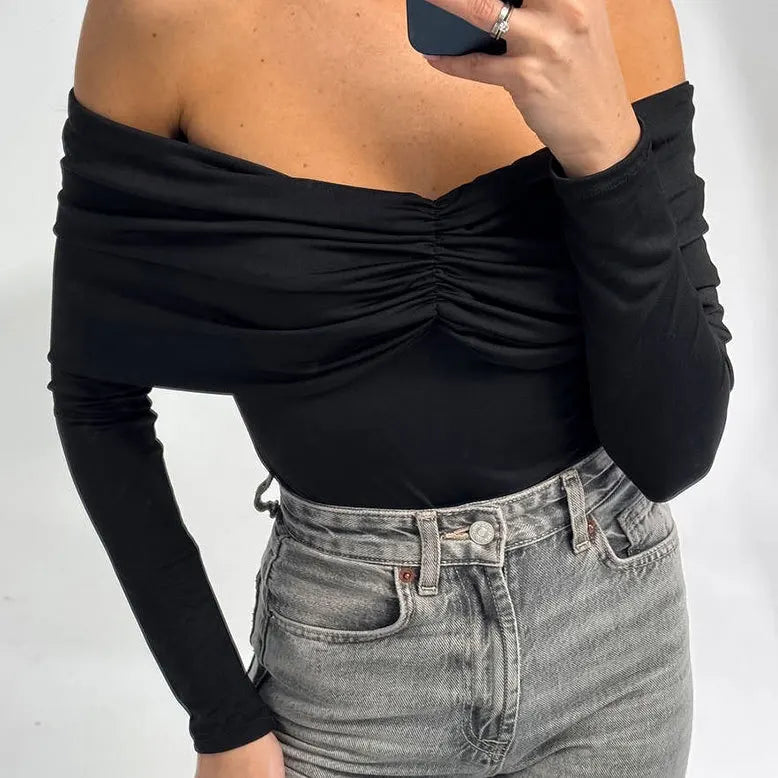 Person wearing a black off-shoulder top and gray jeans on a white background