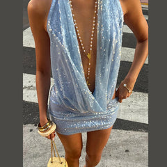 Woman wearing a sparkly blue dress with a necklace, standing on a street.