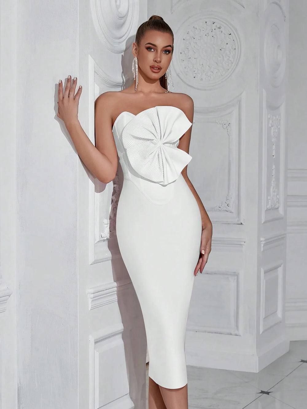 Woman wearing a white strapless dress with a large bow detail in an elegant interior setting.