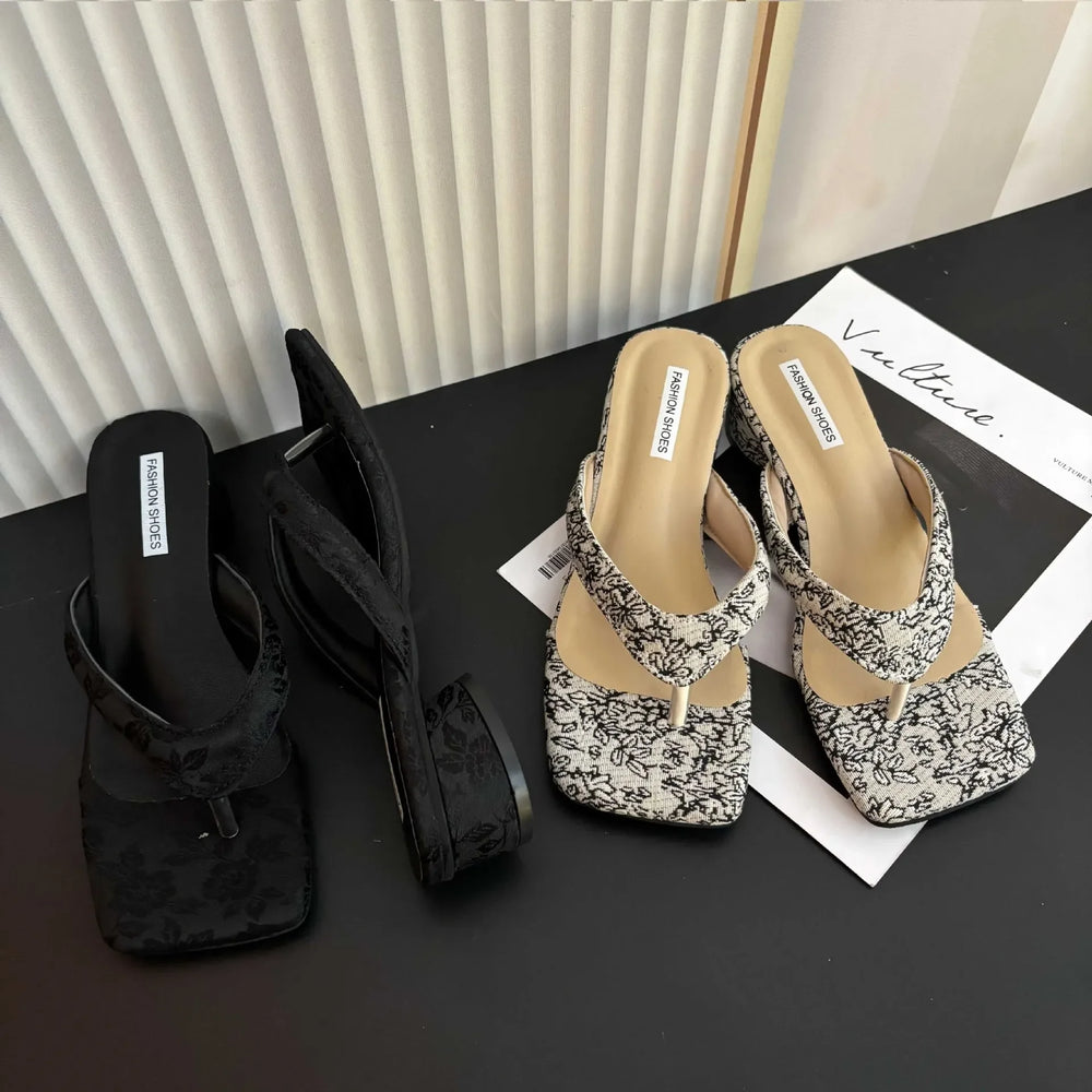 Black and floral-patterned sandals on a black surface with a white background