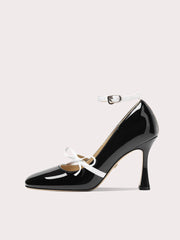 Black patent leather high heel shoe with white laces on a light gray background