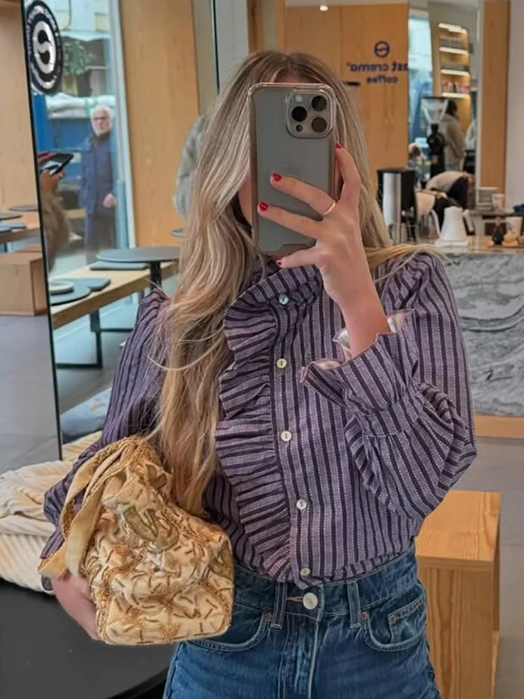 Person taking a mirror selfie wearing a striped shirt and holding a gold bag in a store setting.
