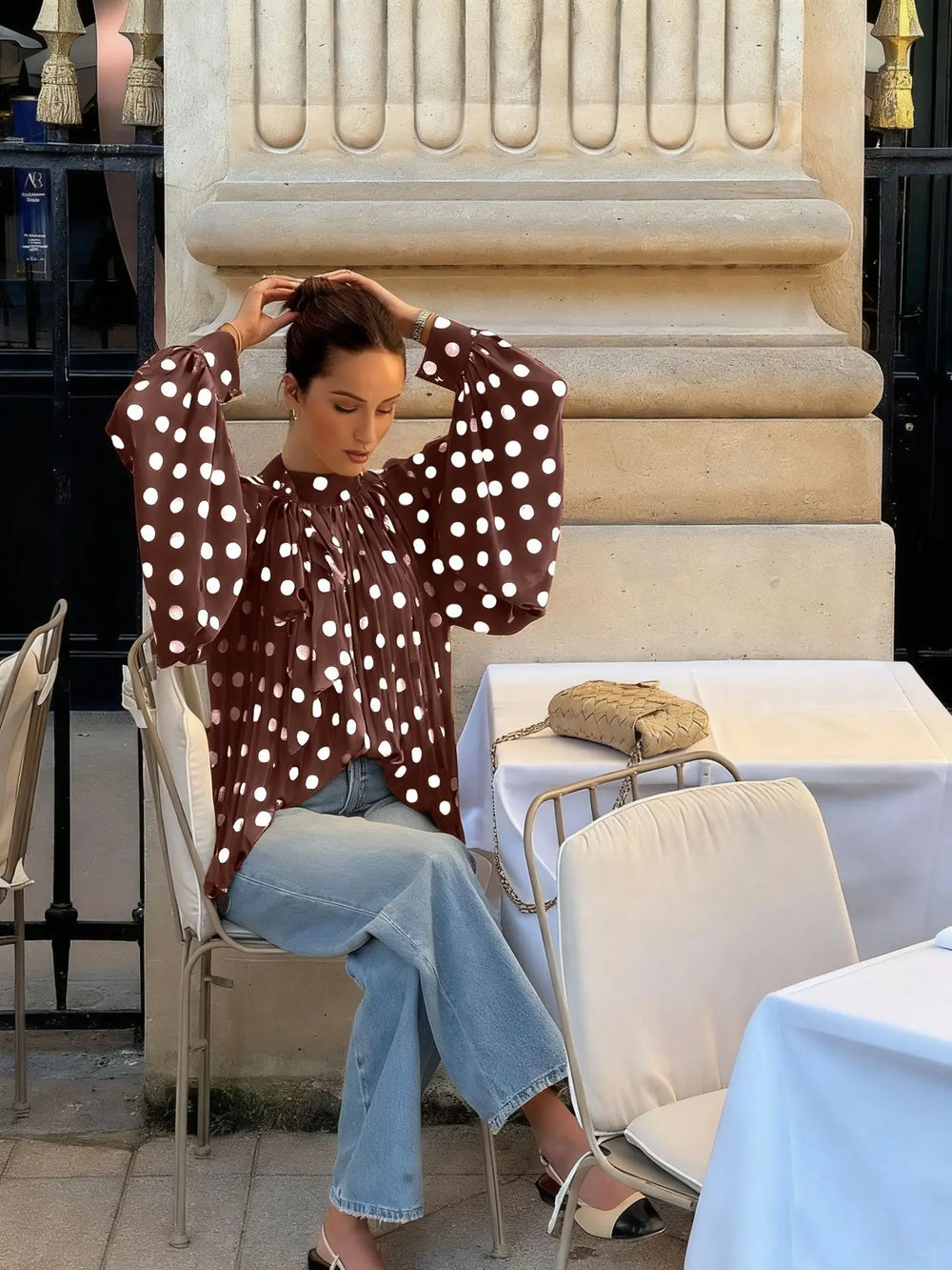 Woman in a polka dot blouse sitting at an outdoor cafe table.