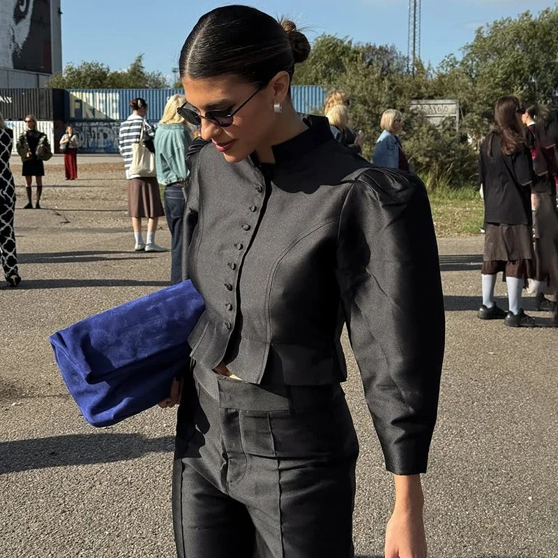 Woman in a black outfit holding a blue clutch with people in the background