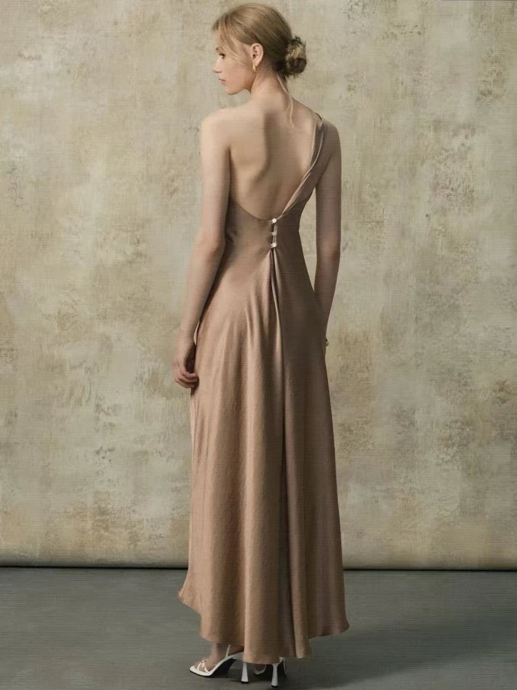 Back view of a woman in a one-shoulder maxi dress showing the open back with buttons