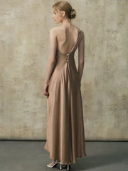 Back view of a woman in a one-shoulder maxi dress showing the open back with buttons