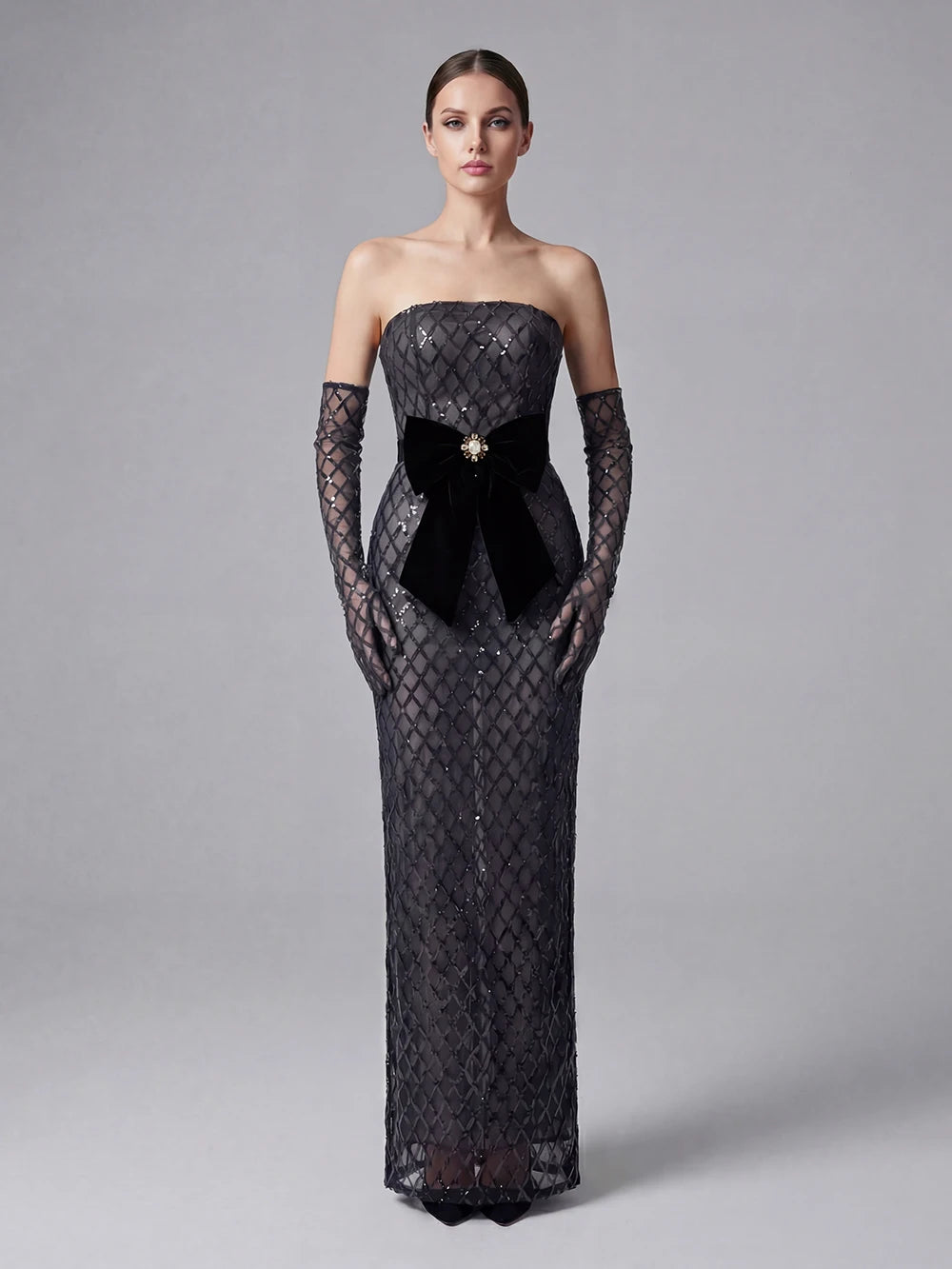 Woman wearing a black strapless evening gown with lace detailing on a gray background