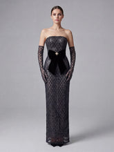 Woman wearing a black strapless evening gown with lace detailing on a gray background