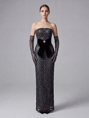 Woman wearing a black strapless evening gown with lace detailing on a gray background