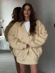 Woman wearing a beige oversized jacket in a minimalistic room.