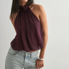Person wearing a burgundy halter top and light blue jeans against a plain background