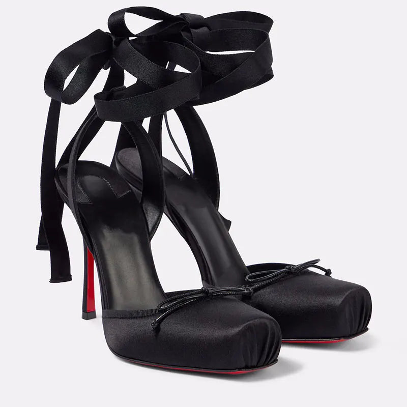 Black high-heeled shoes with ribbon straps on a light gray background