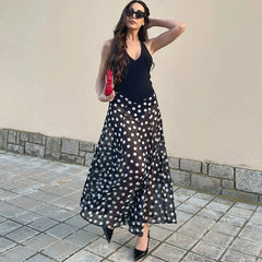 Full body shot of a woman in a polka dot maxi dress with a red clutch.