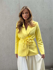 Woman wearing a yellow blazer with a floral detail against a gray background