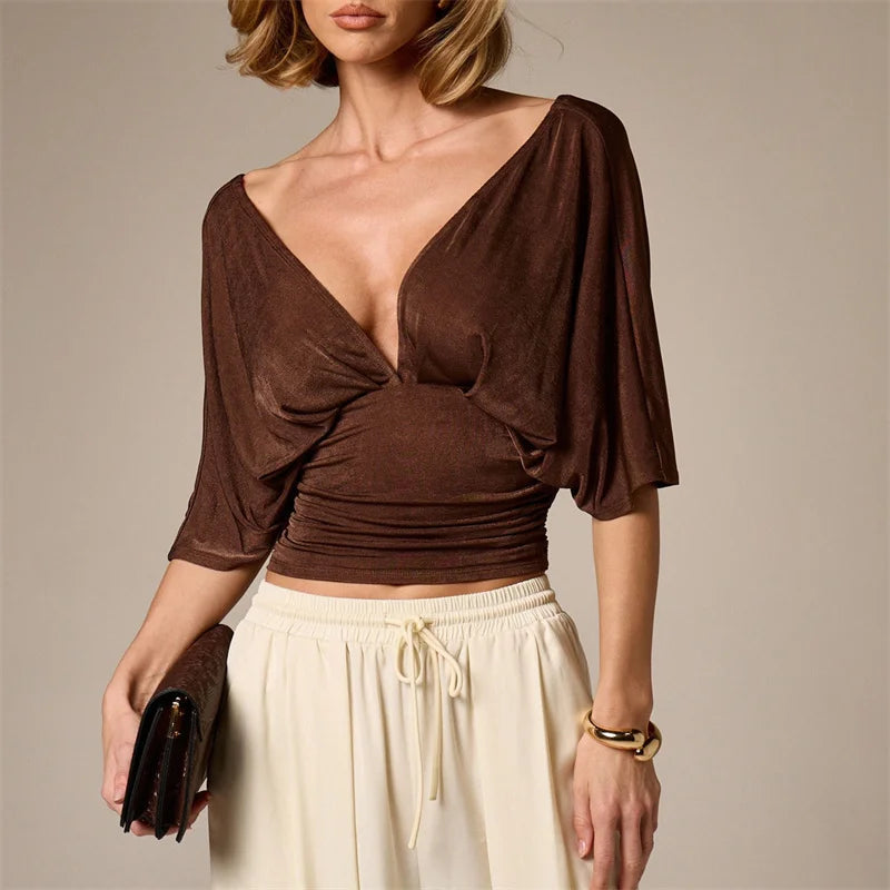 Woman wearing a brown top and white pants against a neutral background