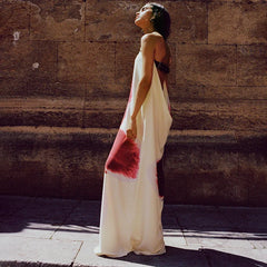 Woman in a long, light-colored dress with red abstract design against a stone wall.