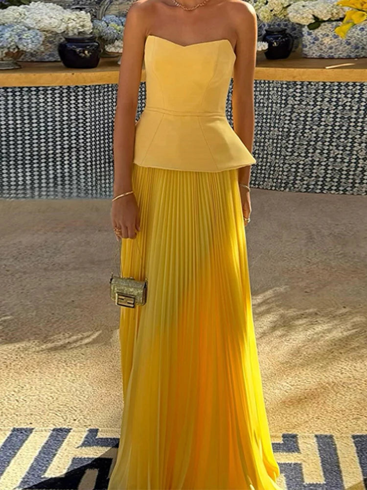 Woman wearing a yellow strapless top and pleated skirt with a blurred background