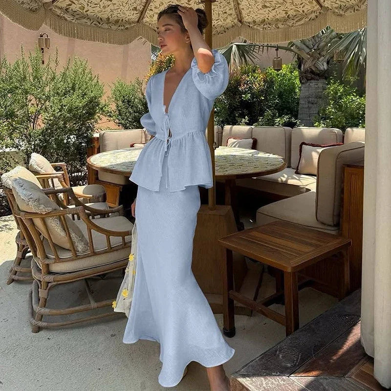 Woman in a light blue dress standing in an outdoor setting with tables and chairs.