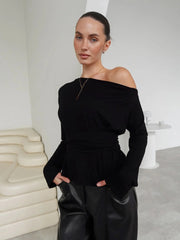 Woman wearing a black off-shoulder top and black pants in a minimalistic setting.