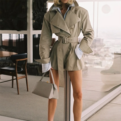 Woman wearing a beige trench coat and holding a matching handbag indoors.