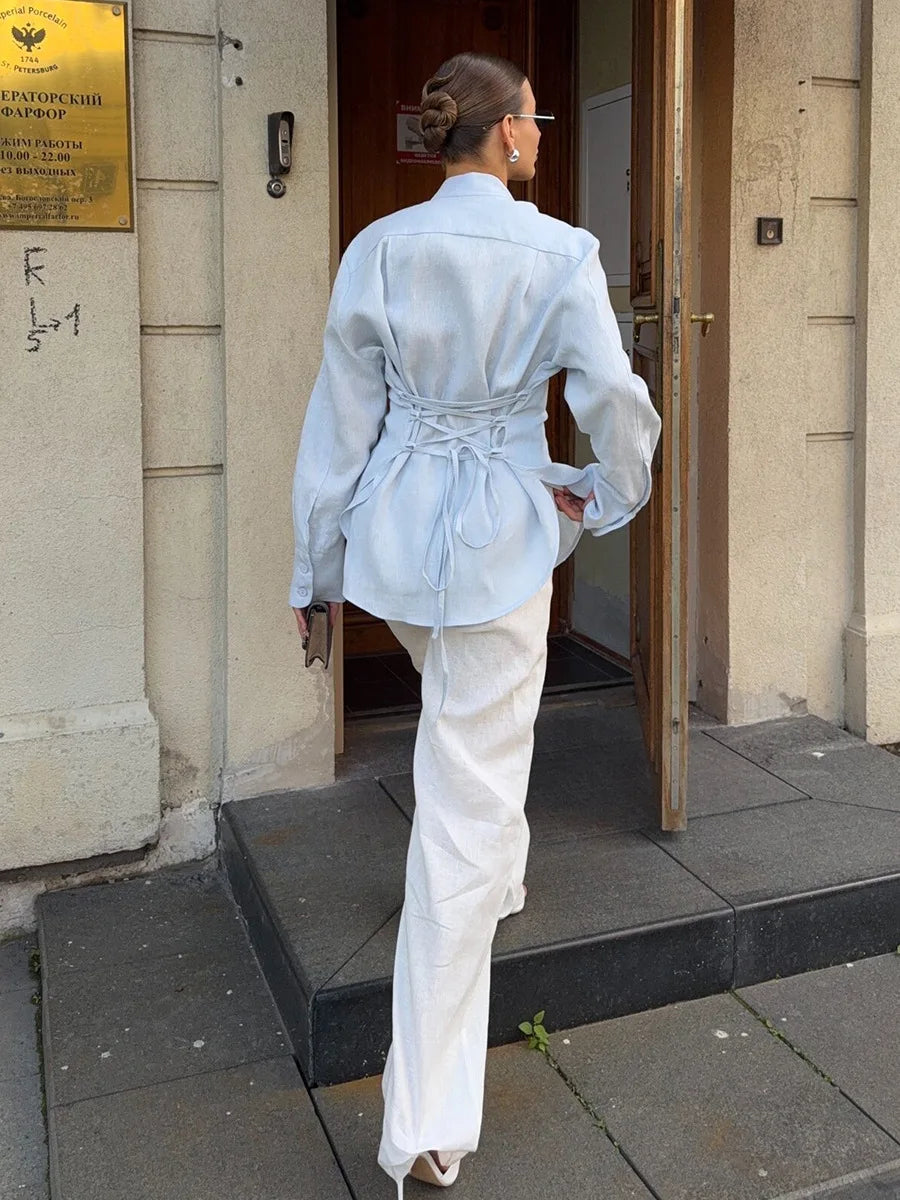 Woman in light blue jacket and white pants exiting a building