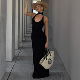 Woman in a black dress and straw hat holding a white bag in a hallway.