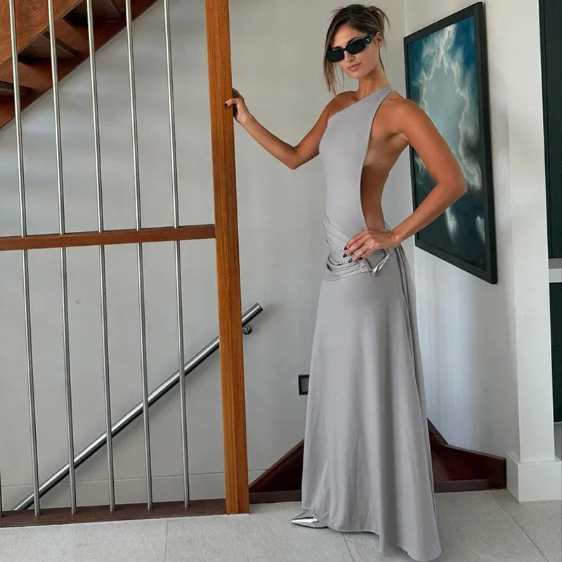 Woman in a gray dress standing indoors with a staircase and wall art in the background