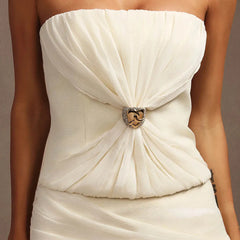 White strapless dress with a decorative brooch on a neutral background