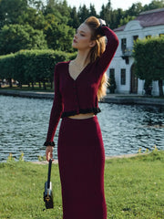 Woman in a burgundy outfit standing by a lake with a building in the background