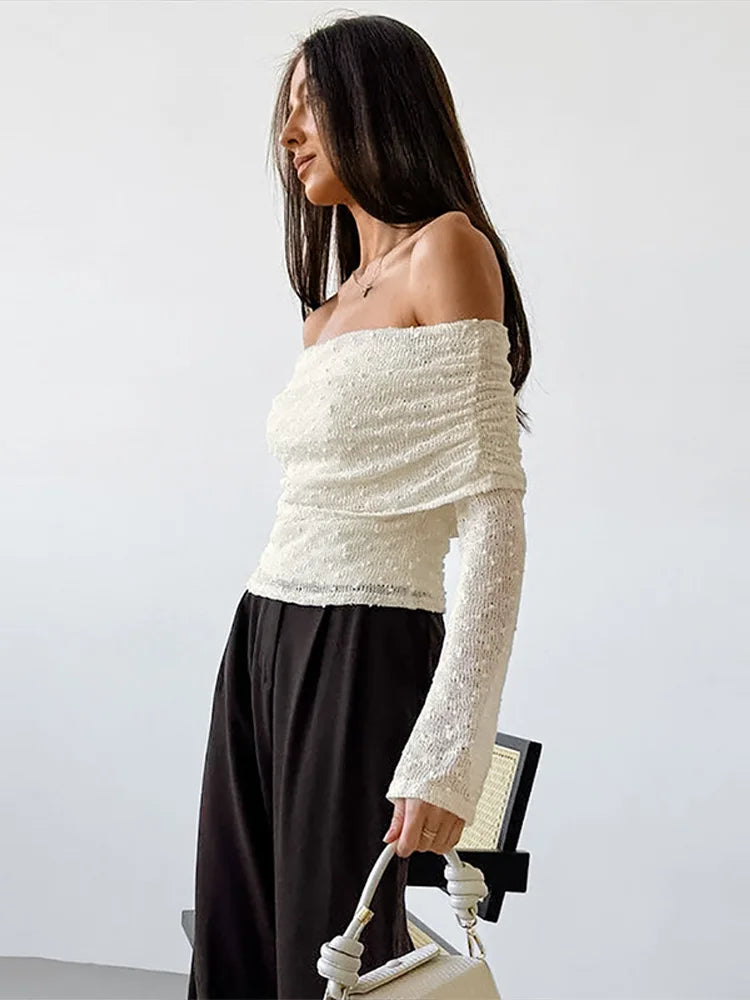 Woman wearing a white off-shoulder top and black pants against a plain background