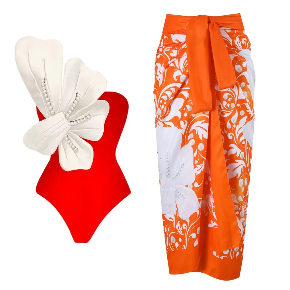 Red one-piece swimsuit with white floral embellishment and pearl details, paired with an orange and white floral wrap skirt.