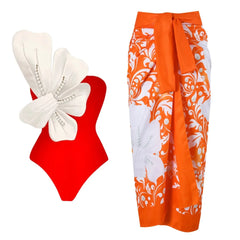 Red one-piece swimsuit with white floral embellishment and pearl details, paired with an orange and white floral wrap skirt.