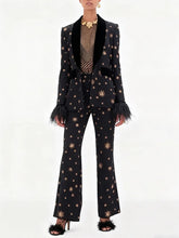 Model wearing a black star embroidered blazer with feather cuffs and matching flare pants.