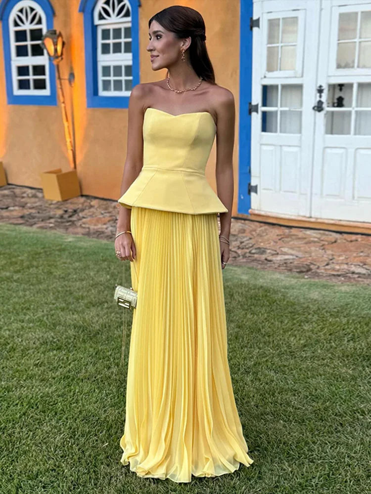 Woman in a yellow strapless dress standing outdoors with a colorful building in the background