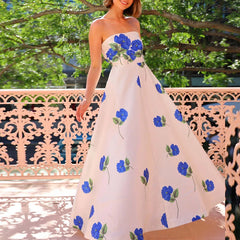 Woman wearing a white dress with blue floral patterns outdoors.