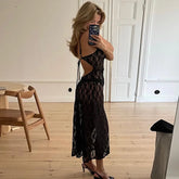 Woman taking a mirror selfie wearing a black lace dress in a room with wooden flooring and white walls.