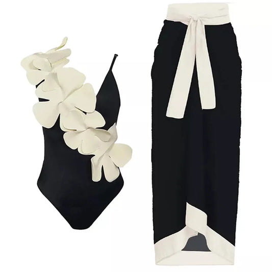 Black one-piece swimsuit with white floral embellishment and a black wrap skirt with white trim.