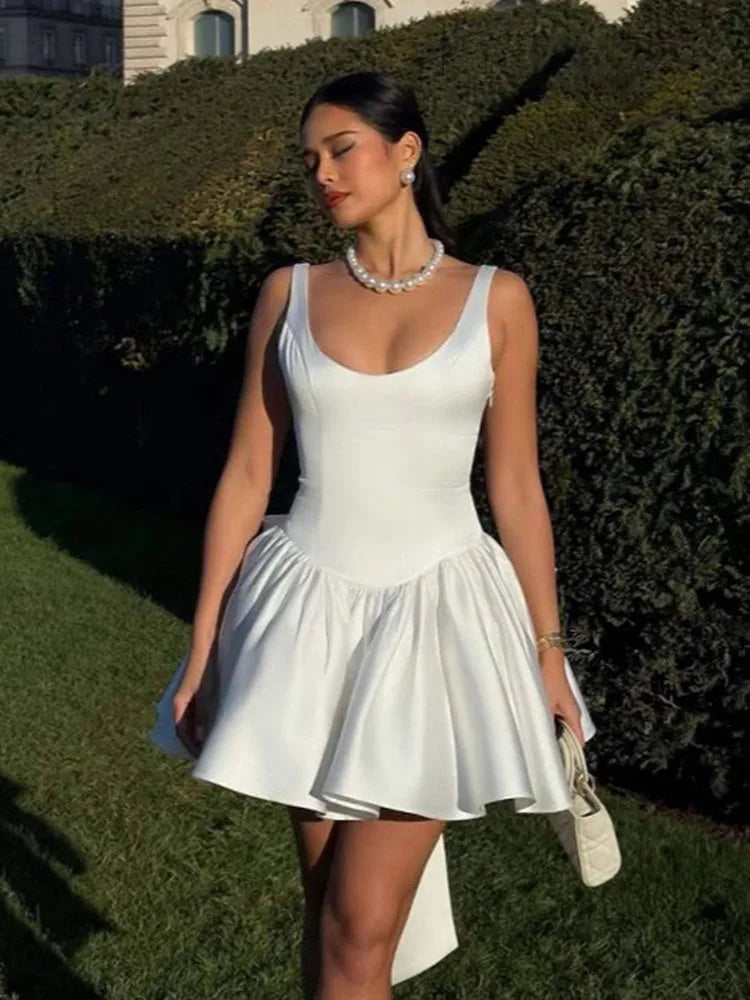Woman wearing a white dress standing outdoors with greenery in the background