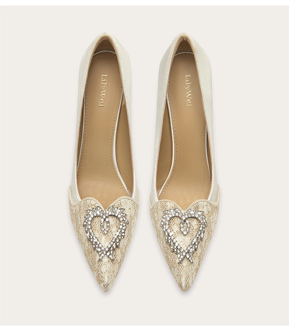 Pair of white pointed-toe shoes with heart-shaped embellishments on a light gray background