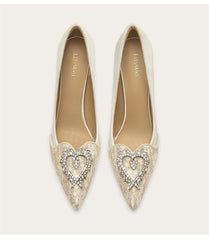 Pair of white pointed-toe shoes with heart-shaped embellishments on a light gray background